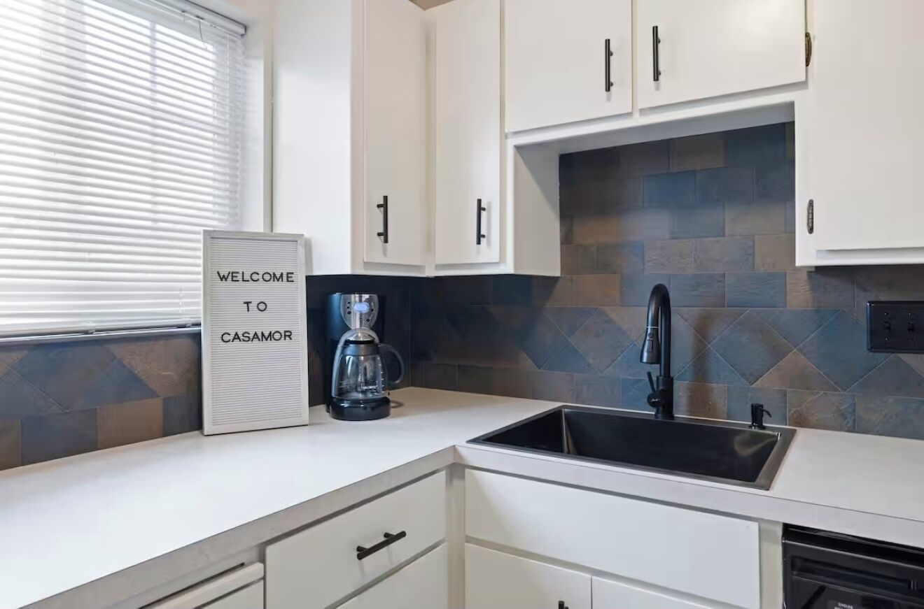 Una cocina moderna con armarios blancos, un lavamanos negro y una cafetera.