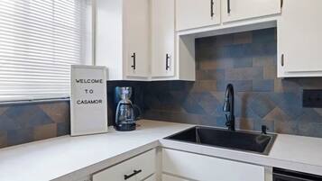 Una cocina moderna con armarios blancos, un lavamanos negro y una cafetera.
