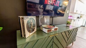 Ett modernt vardagsrum med en platt-TV som visar "NETFLIX", en skivspelare och en hög med Elvis Presleys skivor på ett grönt konsolbord.