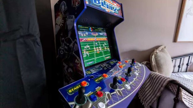 A gaming console with a football game displayed on the screen, surrounded by a bed and a blanket. - Iconic 3BD Entire House in The Heart Of Pittsburg (Pittsburgh)