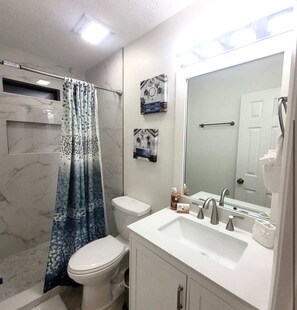 Un baño con inodoro blanco, lavabo blanco y un espejo grande, y cortina de ducha.