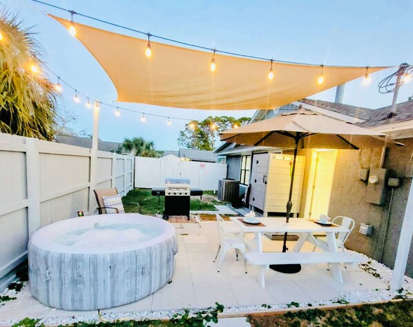 Un patio al aire libre con una zona de estar circular, mesas blancas y un toldo que ofrece sombra.