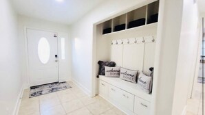 A hallway with a white door, a bench with storage drawers, and a wall-mounted coat rack with hooks. - Stunning 4BD Jacuzzi - 4 Min To Beach Panama City (Panama City Beach)