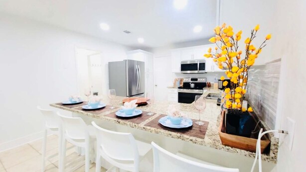 A modern kitchen with white cabinets, a stainless steel refrigerator, and a microwave. - Stunning 4BD Jacuzzi - 4 Min To Beach Panama City (Panama City Beach)