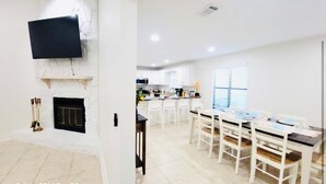 A modern living room with a flat-screen TV mounted on a white wall, a fireplace, and a dining area with a table and chairs. - Stunning 4BD Jacuzzi - 4 Min To Beach Panama City (Panama City Beach)
