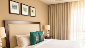 Habitación de hotel con una cama grande, dos mesitas de noche con lámparas, una mesita con teléfono y una ventana con cortinas.