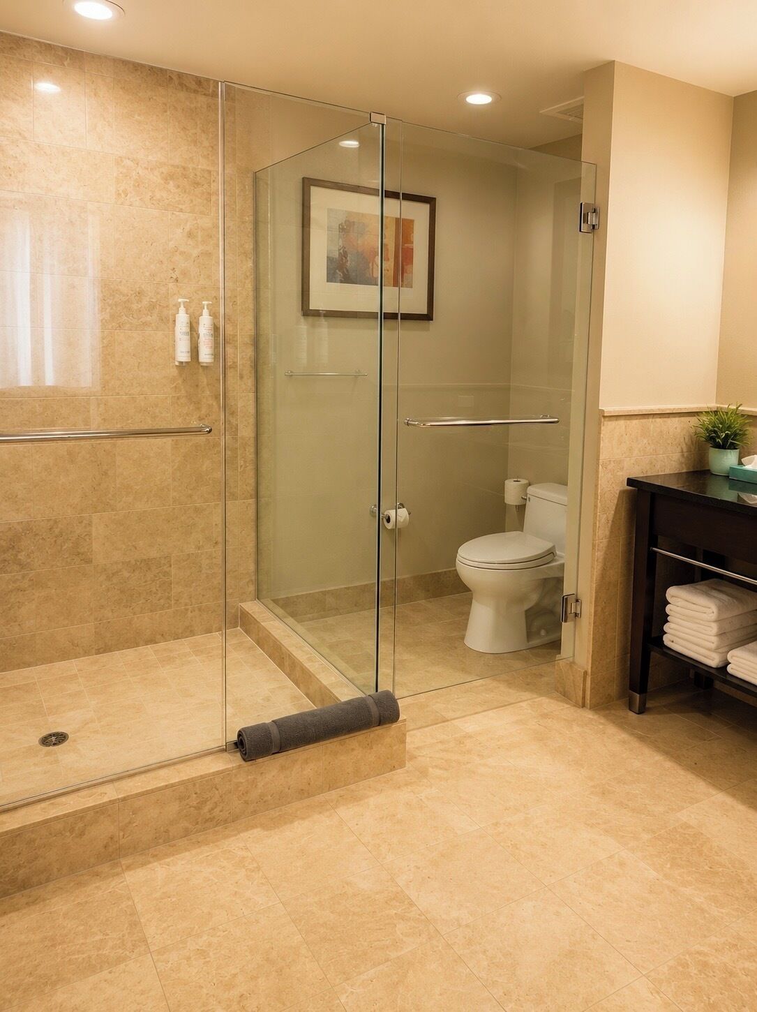 A modern bathroom with a glass-enclosed shower, a toilet, and a sink area with towels.