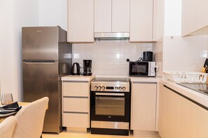 Una cocina compacta con refrigerador de acero inoxidable, cafetera, microondas y estufa.