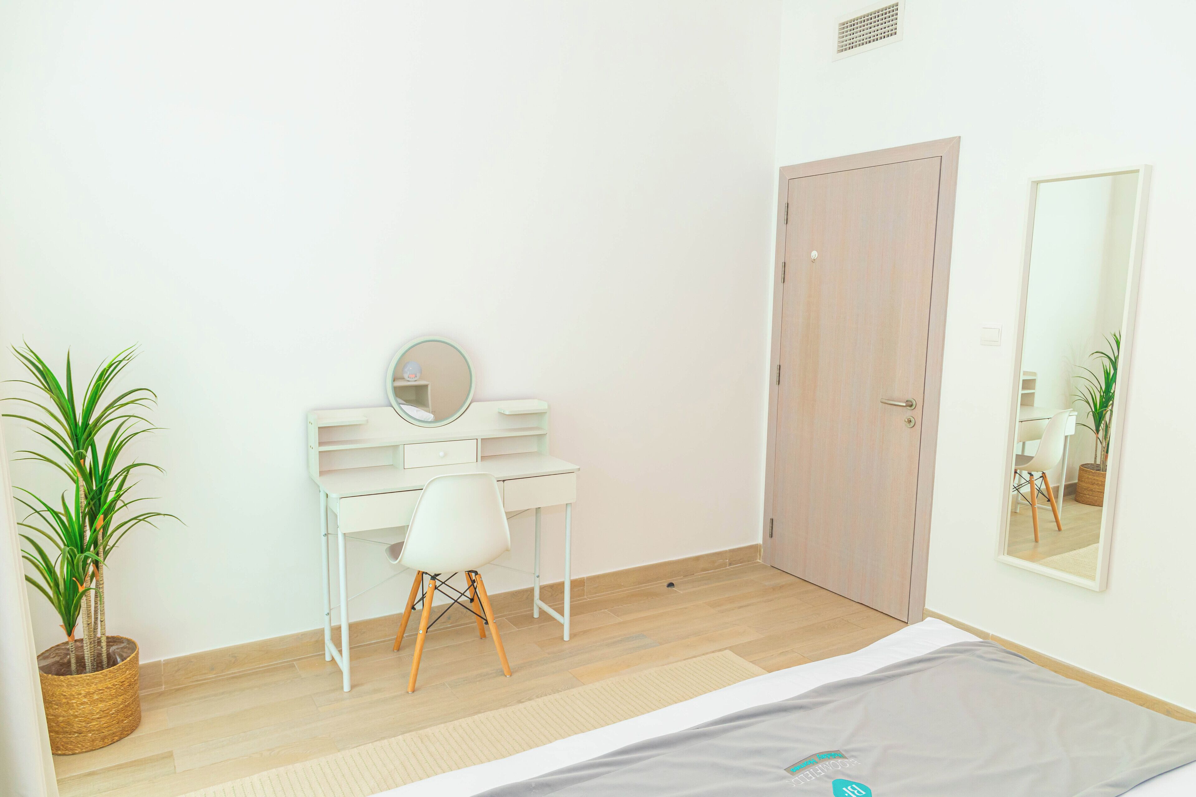 A bedroom with a bed, a desk, a chair, a mirror, and a door.