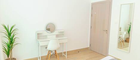 A bedroom with a bed, a desk, a chair, a mirror, and a door.