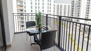A balcony with a glass table and chairs, a potted plant, and a view of surrounding buildings. - Bloomfields Stylish 1BR in Waters Edge (Abu Dhabi)