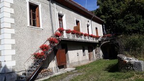 A stone building with a balcony adorned with red flowers, a wooden door, and a stone wall.