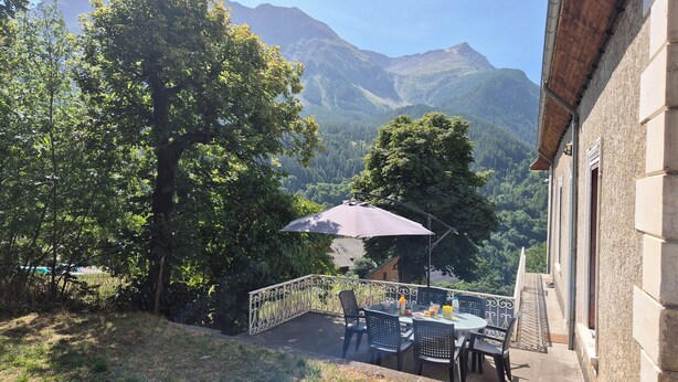 A patio with a table and chairs, surrounded by trees and a mountain view.