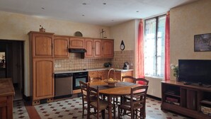 A kitchen with wooden cabinets, a dining table with chairs, a built-in oven, and a television on a wooden stand.