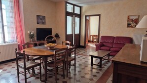 A dining area with a wooden table and chairs, a red sofa, and a television on the wall.