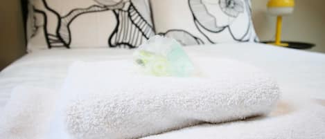 Una cama bien hecha con una toalla blanca y otra toalla doblada encima.