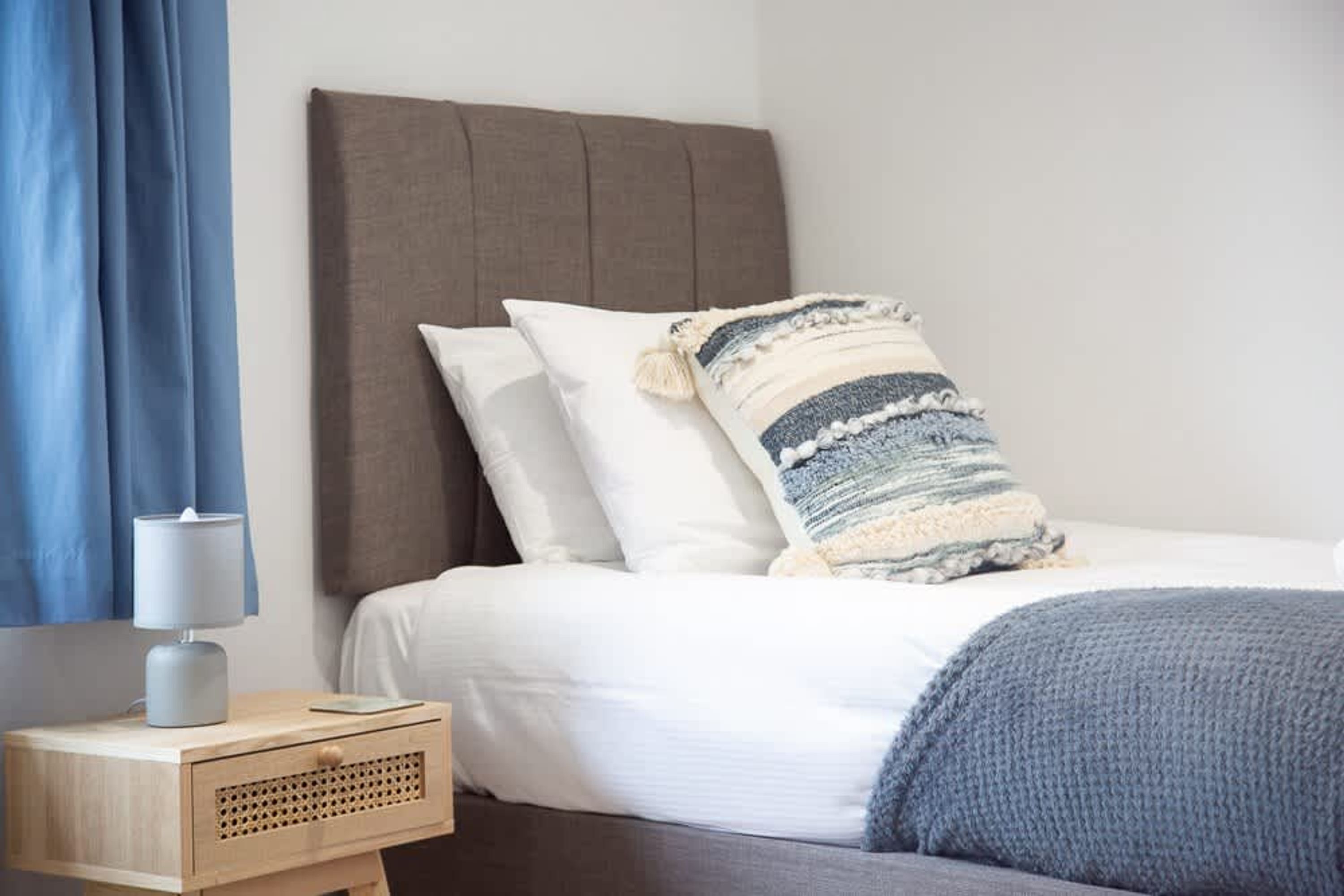 A neatly made bed with a striped throw blanket, a bedside lamp, and a wooden nightstand with a lamp.