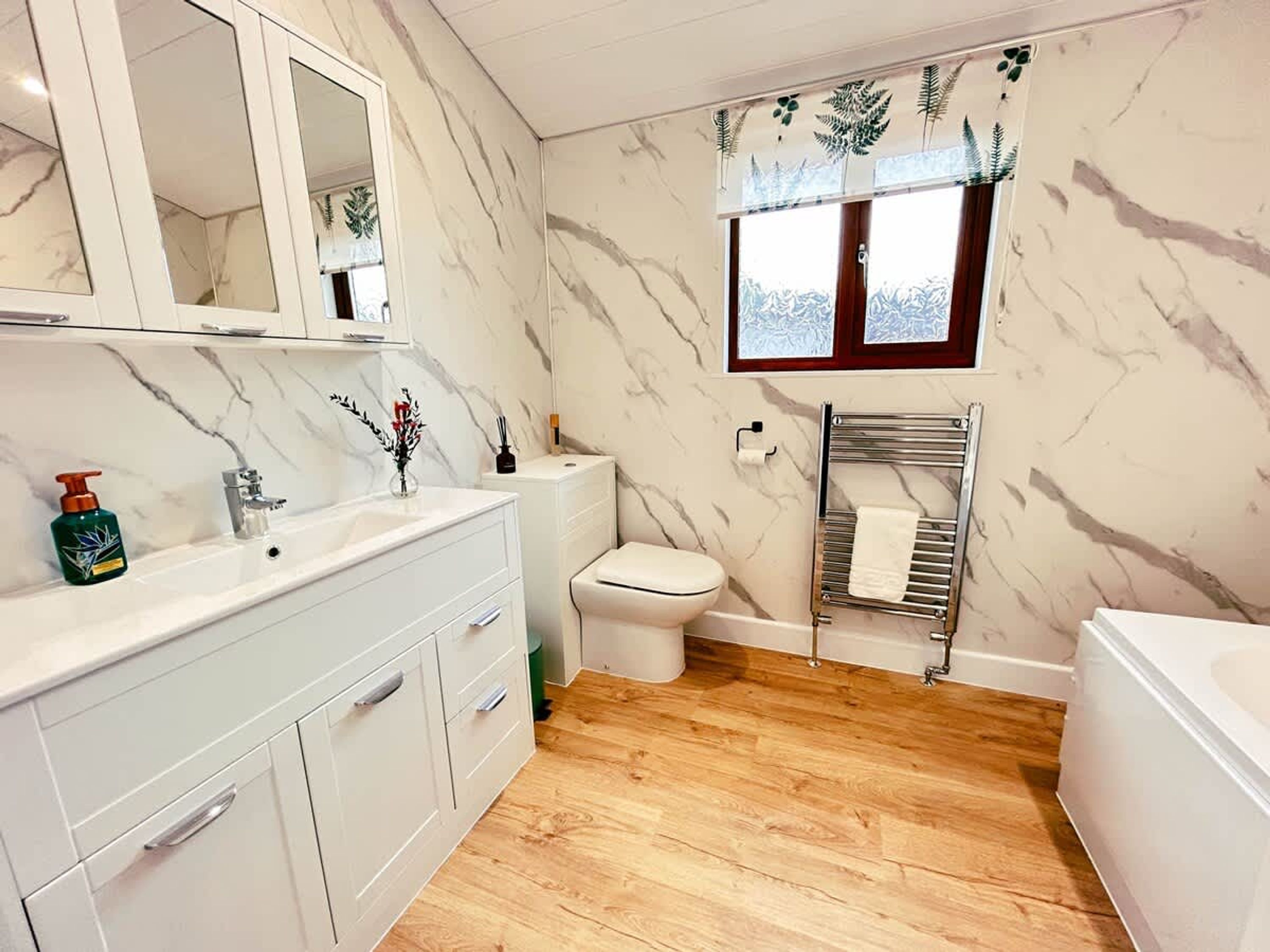 A bathroom with a marble wall, a wooden floor, a white sink, a toilet, and a bathtub.
