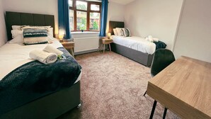 Ein Schlafzimmer mit zwei Betten, einem Holztisch und einem Fenster mit Vorhängen.