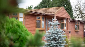 Ein Holzhaus mit Ziegeldach, einer sichtbaren Haustür und einem kleinen Baum im Vordergrund.