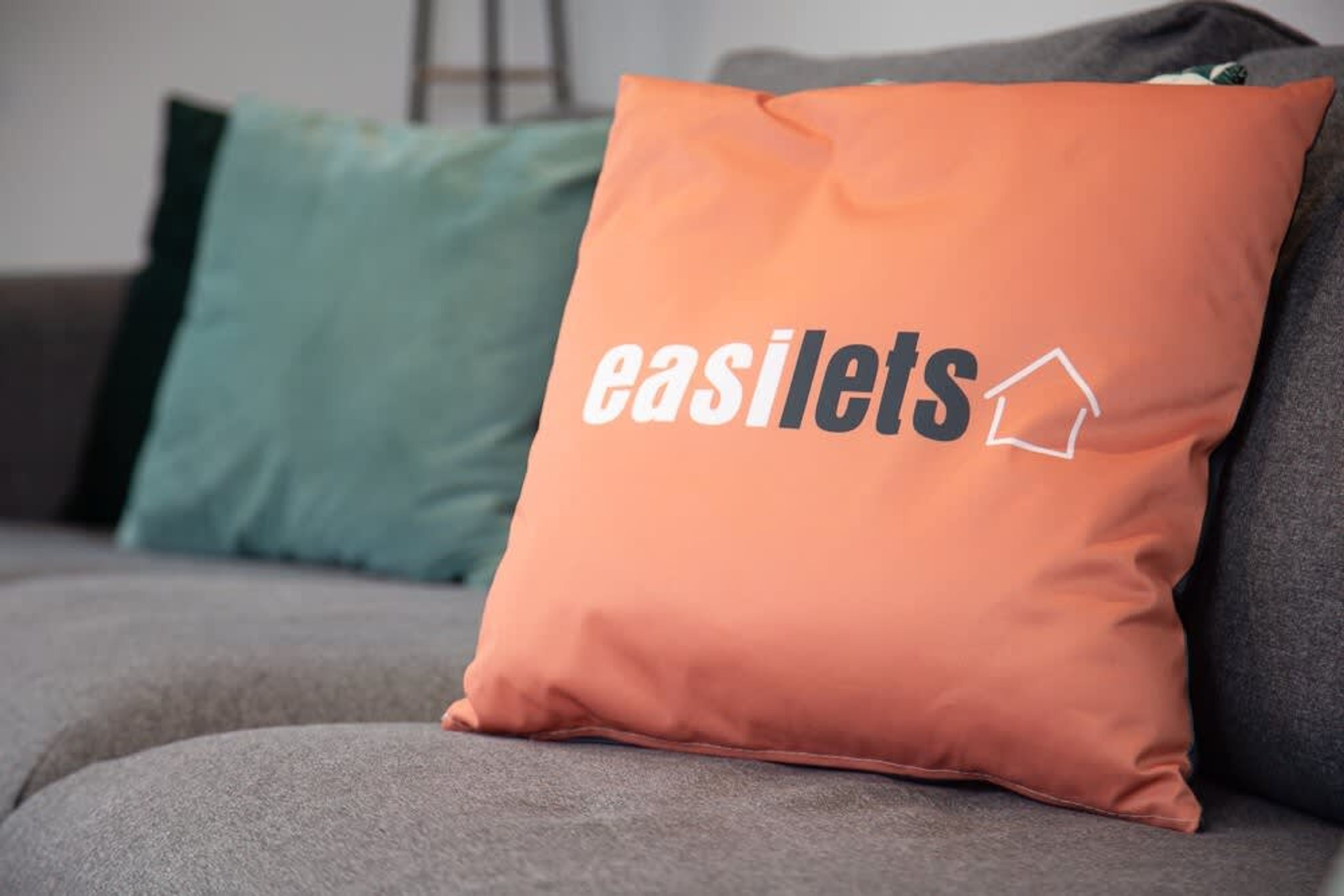 A cushion with the text "easilets" and a house icon on a grey sofa.