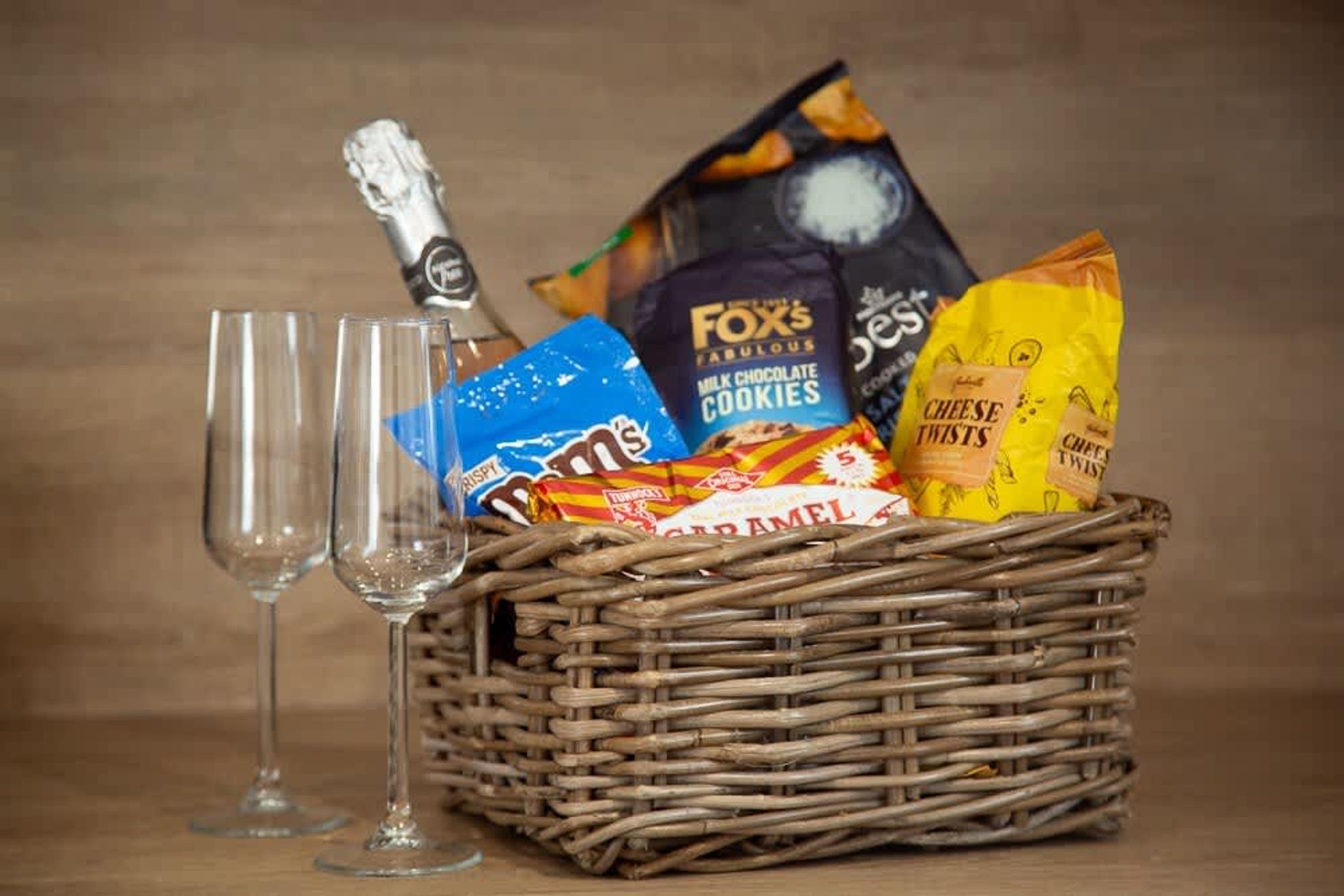 Una cesta de mimbre con aperitivos y una botella de champán, junto a dos copas vacías.