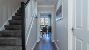 Un pasillo con escaleras alfombradas, un comedor con sillas y una mesa, y una puerta con un marco de cuadro.