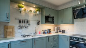 Una cocina moderna con armarios azul verdoso, microondas, horno y diversos utensilios.