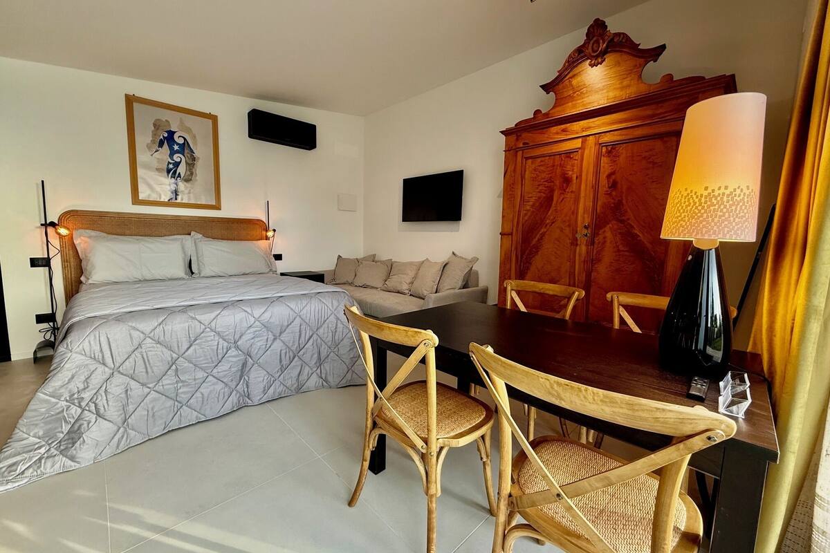 A hotel room with a bed, a sofa, a wooden cabinet, a table with chairs, and a TV mounted on the wall.