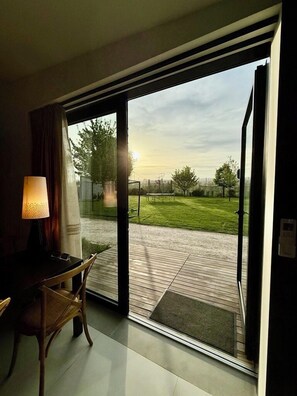 Una stanza con un'ampia porta-finestra scorrevole che si apre su un patio con prato e terrazza in legno.