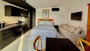 A compact bedroom with a bed, bedside table, and a sofa. A kitchenette with a stove and sink is adjacent to the bed. - Memento Agriturismo (Cervia)