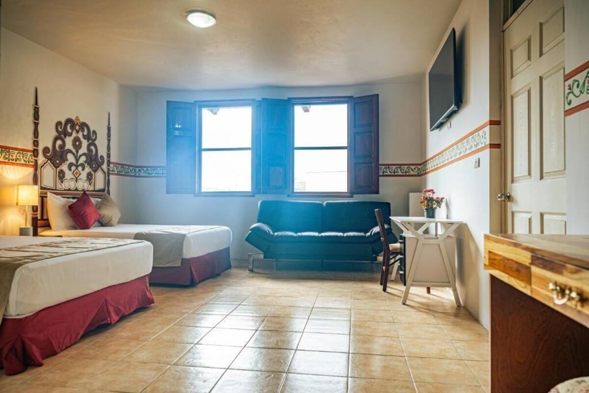 Ein Zimmer mit zwei Betten, einem Schlafsofa, einem kleinen Tisch, einem Fernseher und einem Fenster mit geöffneten Fensterläden.