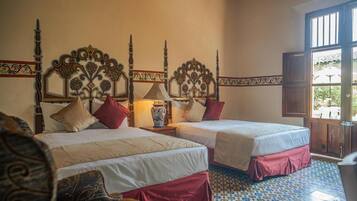 A hotel room with two beds, ornate headboards, a tiled floor, and a view through an open door.