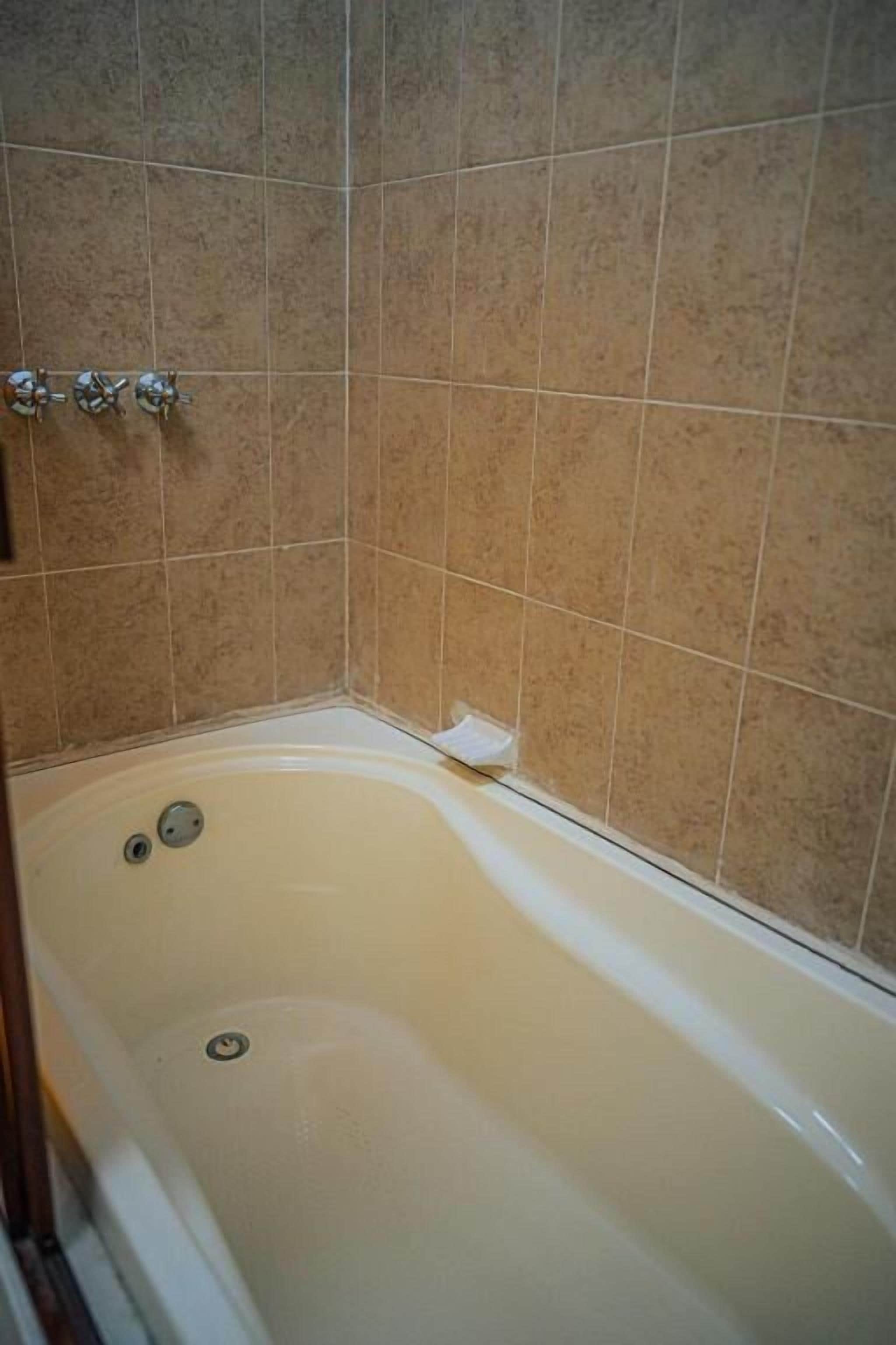 Et badeværelse med badekar, beige flisevægge og et hvidt badekar.