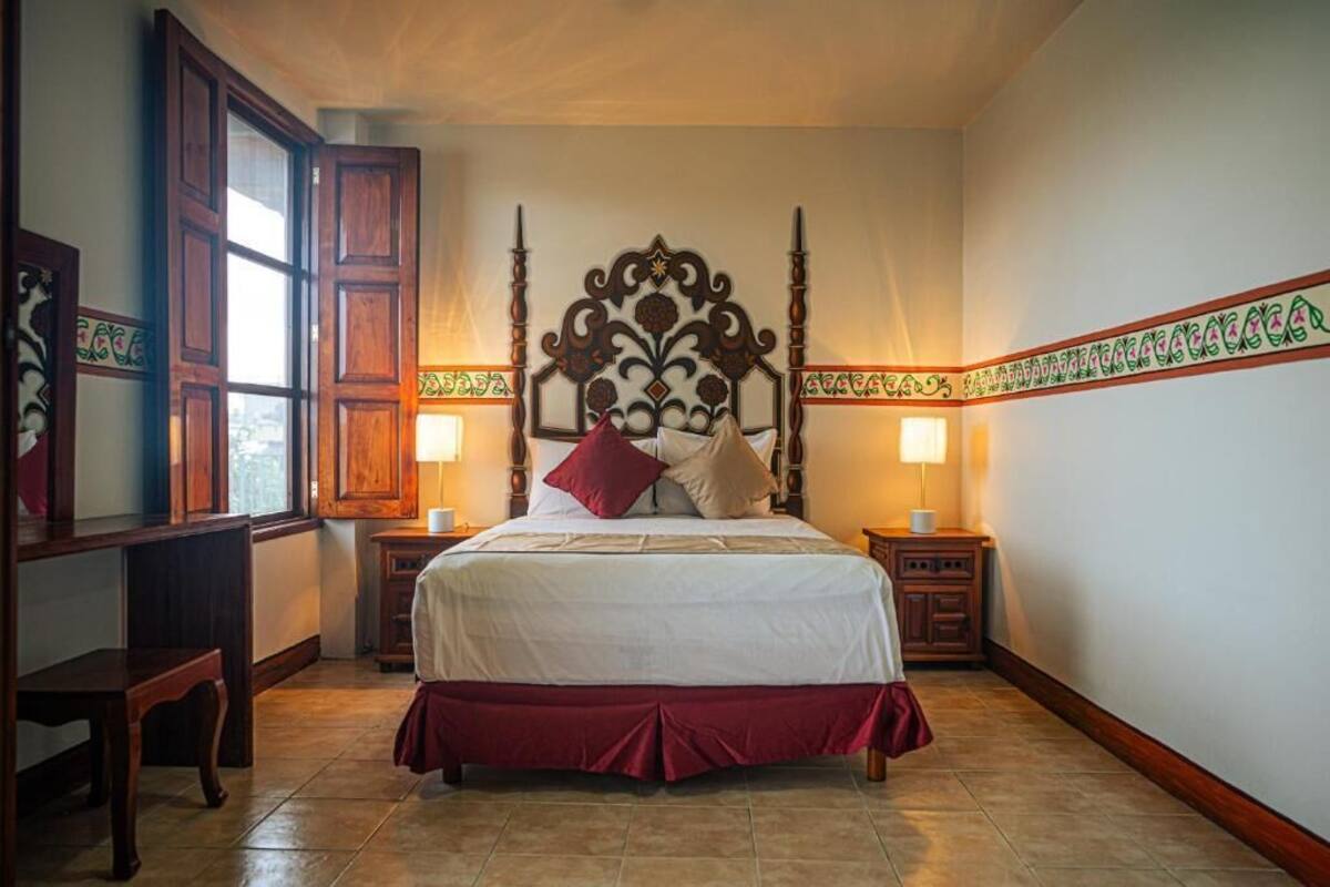 Ein Schlafzimmer mit einem großen Bett, einem Holz-Kopfstück, zwei Nachttischen und einem Fenster mit Holzjalousien.