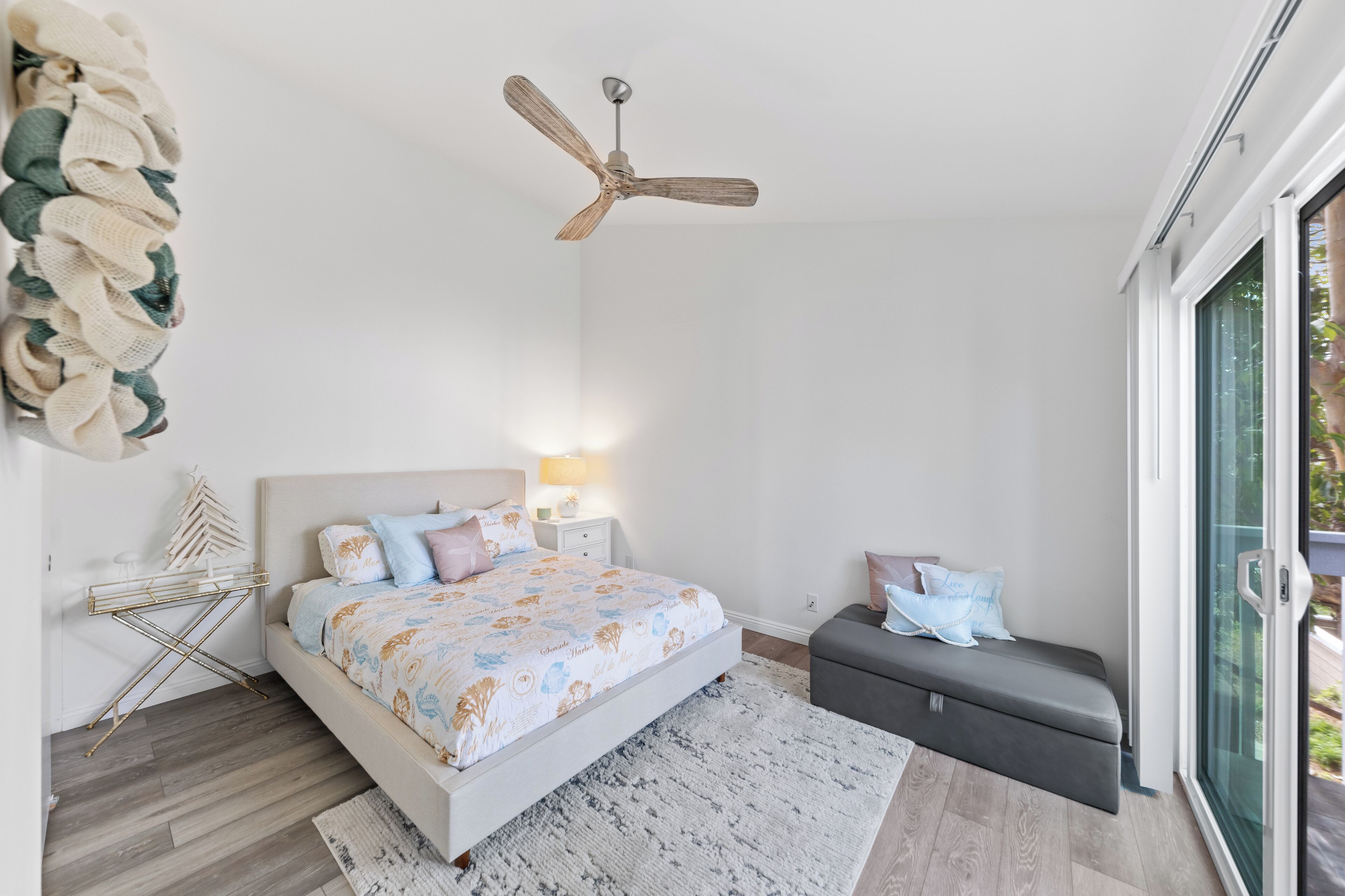 Une chambre moderne avec un lit, des tables de chevet, un banc, un ventilateur de plafond et une grande fenêtre.