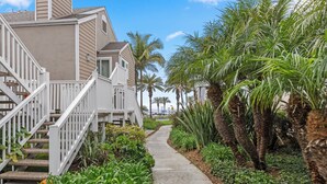 A residential area with a concrete pathway, white railings, and lush greenery including palm trees. - Charming Beach condo on the Shores at Strand Beach (Dana Point)