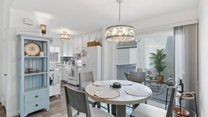 A modern kitchen with white cabinets, a blue cabinet, and a dining area with a round table and chairs. - Charming Beach condo on the Shores at Strand Beach (Dana Point)