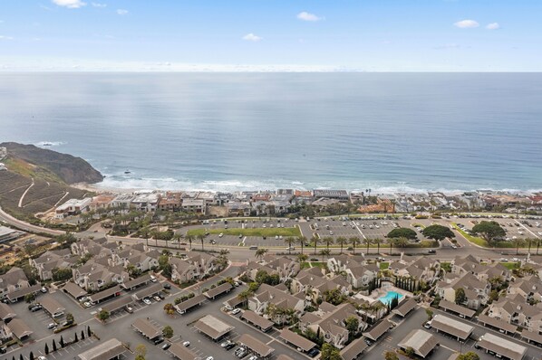 Vue aérienne d’une zone résidentielle côtière, avec des maisons, des routes et une plage.