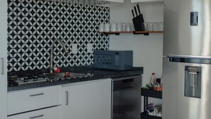 Et moderne køkken med hvide skabe, et sort-hvidt baggrundsmønster, et rustfrit stål køleskab og en mikrobølgeovn på bordpladen.