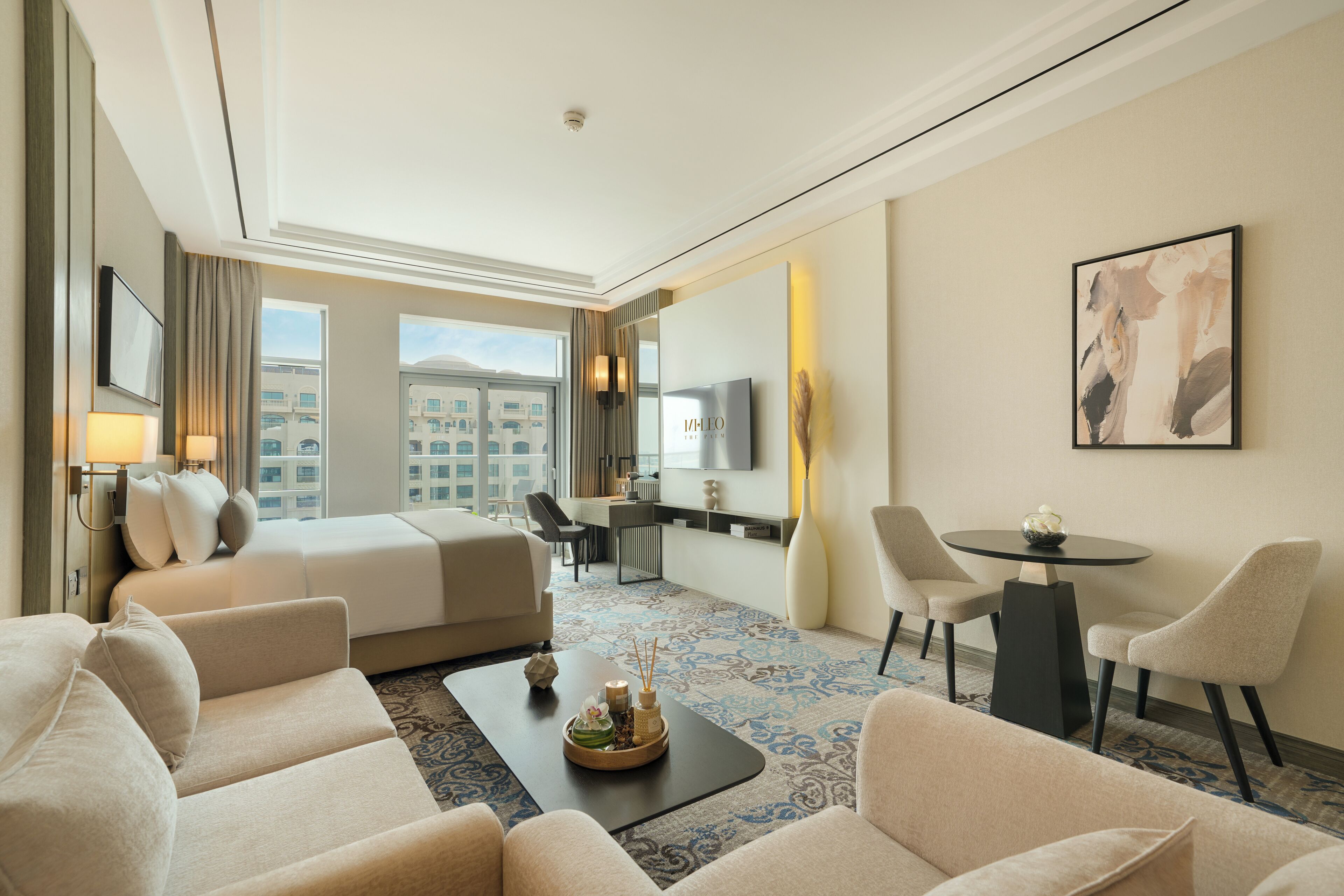 A hotel room with a bed, two sofas, a desk, a dining table, and a large window with a city view.
