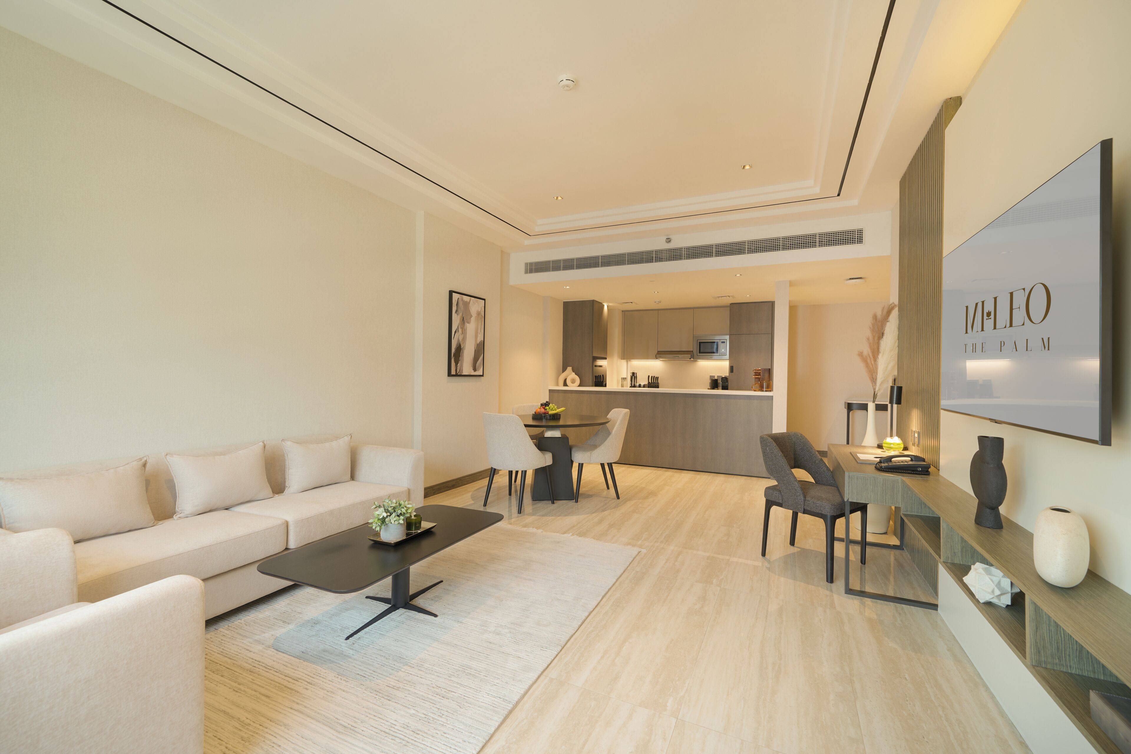 A modern living room with a sofa, coffee table, and chairs. There is a kitchen area with a dining table and chairs. A large framed artwork is on the wall.