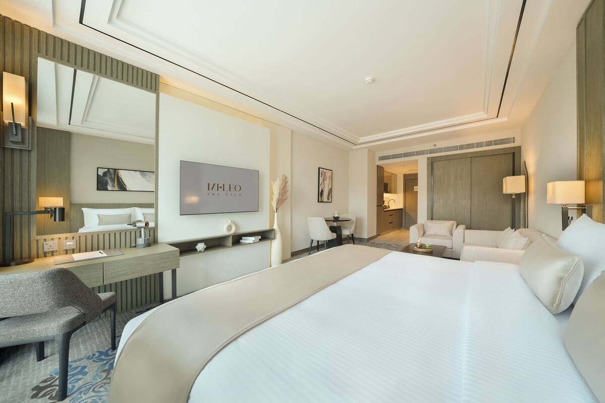 A modern hotel room with a large bed, a desk, a chair, and a sofa.