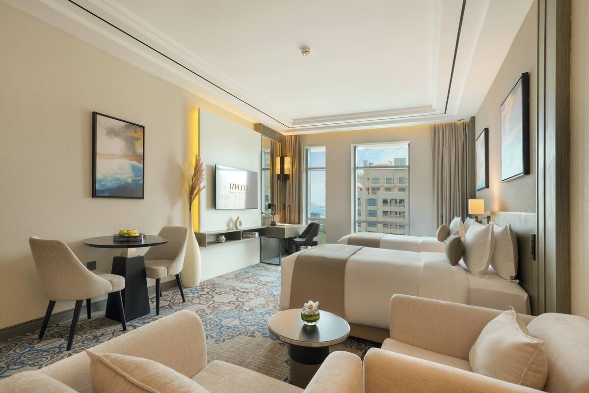 A hotel room with a large bed, two armchairs, a small table, a desk, and a TV.