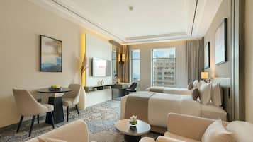 A hotel room with a bed, two armchairs, a small table, a desk, a TV, and a window with a city view.