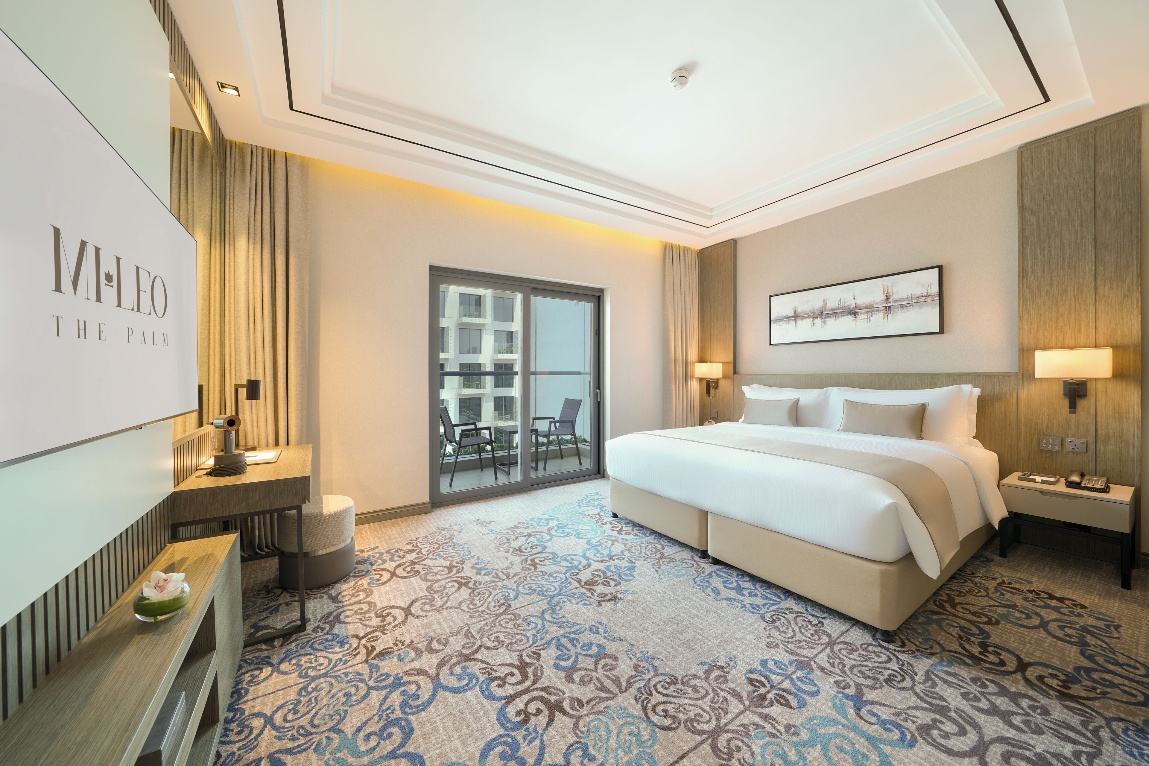 A hotel room with a large bed, a desk, a chair, a TV, and a balcony with a view of the city.