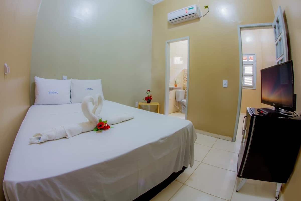 A hotel room with a bed, a TV, and an air conditioning unit.