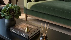 En moderne stue med en grøn sofa, en lampe, en bog med titlen "CALL IT HOME" og en vase med rør.