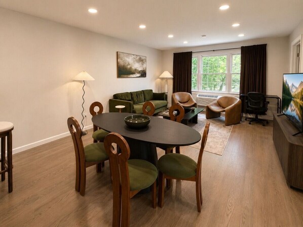 Un salon moderne comprenant une table à manger, des chaises, un canapé et un téléviseur.