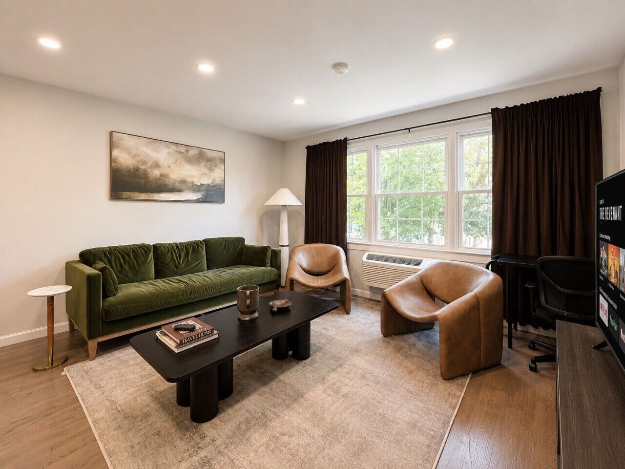 Una sala de estar moderna con un sofá verde, una mesa de centro, un sillón de cuero marrón, una lámpara y un televisor.